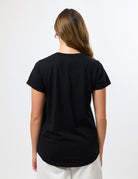 A woman viewed from the back wearing a plain black short-sleeve t-shirt and off-white pants against a clean white studio background.