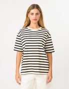 A woman modeling a short-sleeve crewneck t-shirt with horizontal black and off-white stripes, paired with off-white shorts, against a plain white studio background.