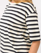 A close-up of a person wearing a short-sleeve top with horizontal black and off-white stripes, cropped from the shoulders to the waist against a plain light background.