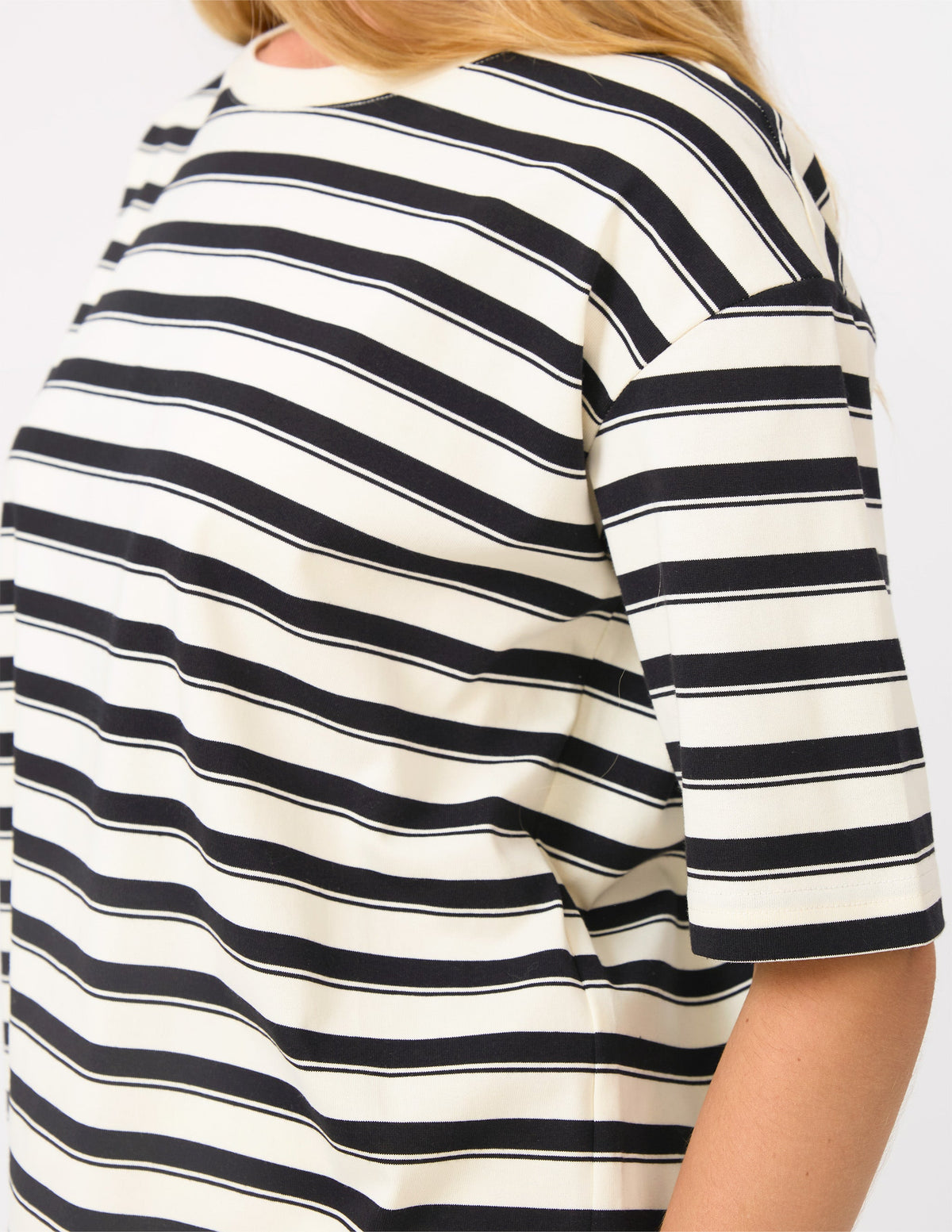 A close-up of a person wearing a short-sleeve top with horizontal black and off-white stripes, cropped from the shoulders to the waist against a plain light background.