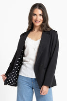 Woman wearing a black blazer over a white top with polka dot sleeves on a white background