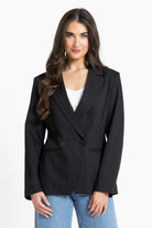 Woman wearing a black blazer over a white top and blue jeans on a white background