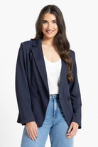 Woman wearing a navy blazer over a white top and blue jeans on a white background