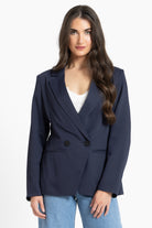 Woman wearing a navy blazer over a white top and blue jeans on a white background