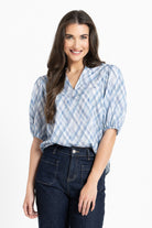 A woman modeling a light blue and white checkered puff-sleeve blouse tucked into dark blue jeans, set against a plain white studio background.