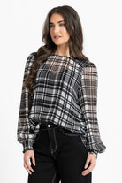 A woman modeling a sheer long-sleeve blouse with a black, white, and gray plaid pattern and balloon sleeves, paired with black pants, against a plain white studio background.