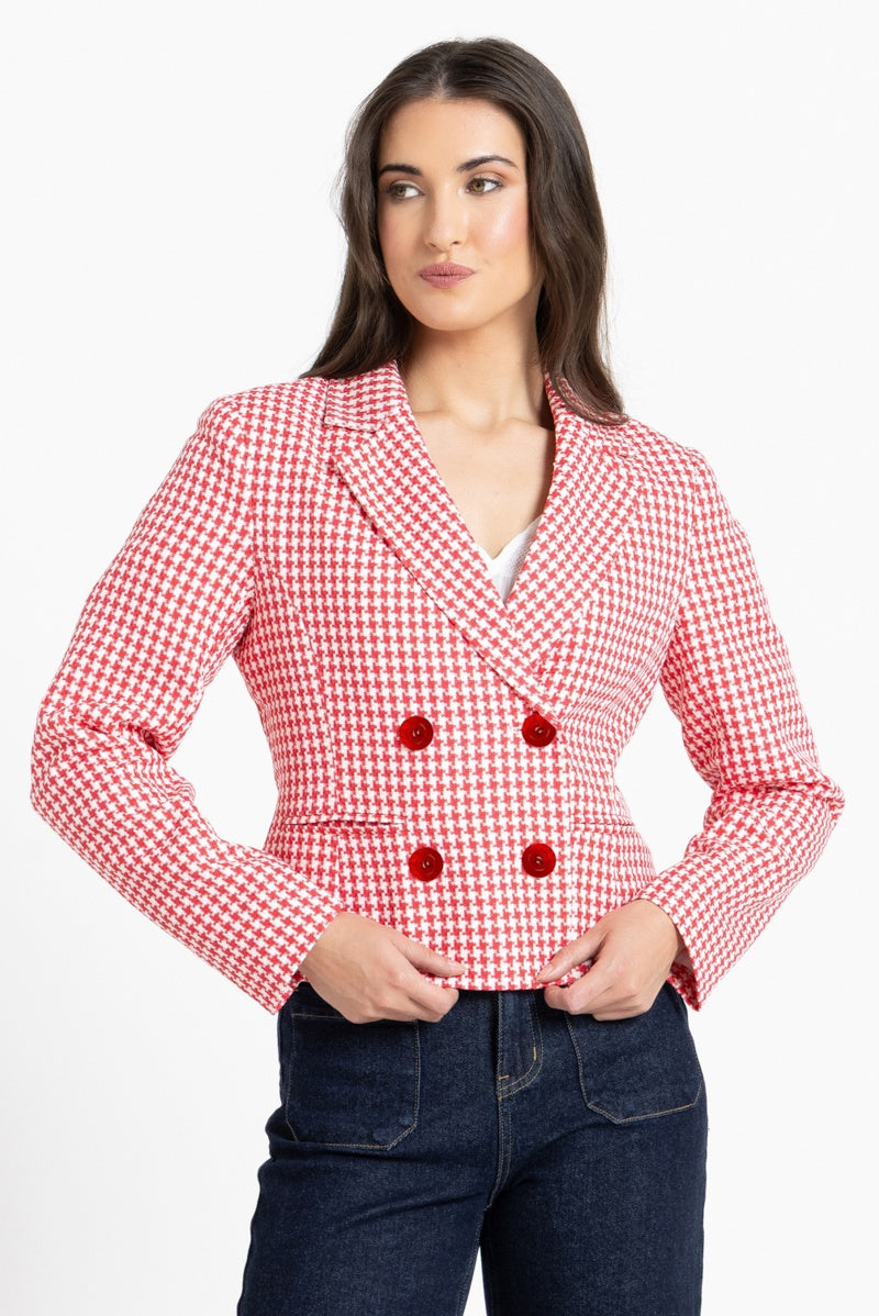 A woman modeling a red and white gingham double-breasted blazer with red buttons, paired with dark blue jeans, against a plain white background.