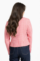 A woman viewed from the back wearing a red and white houndstooth patterned blazer and dark blue jeans against a plain white background.