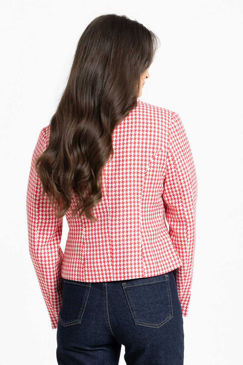 A woman viewed from the back wearing a red and white houndstooth patterned blazer and dark blue jeans against a plain white background.