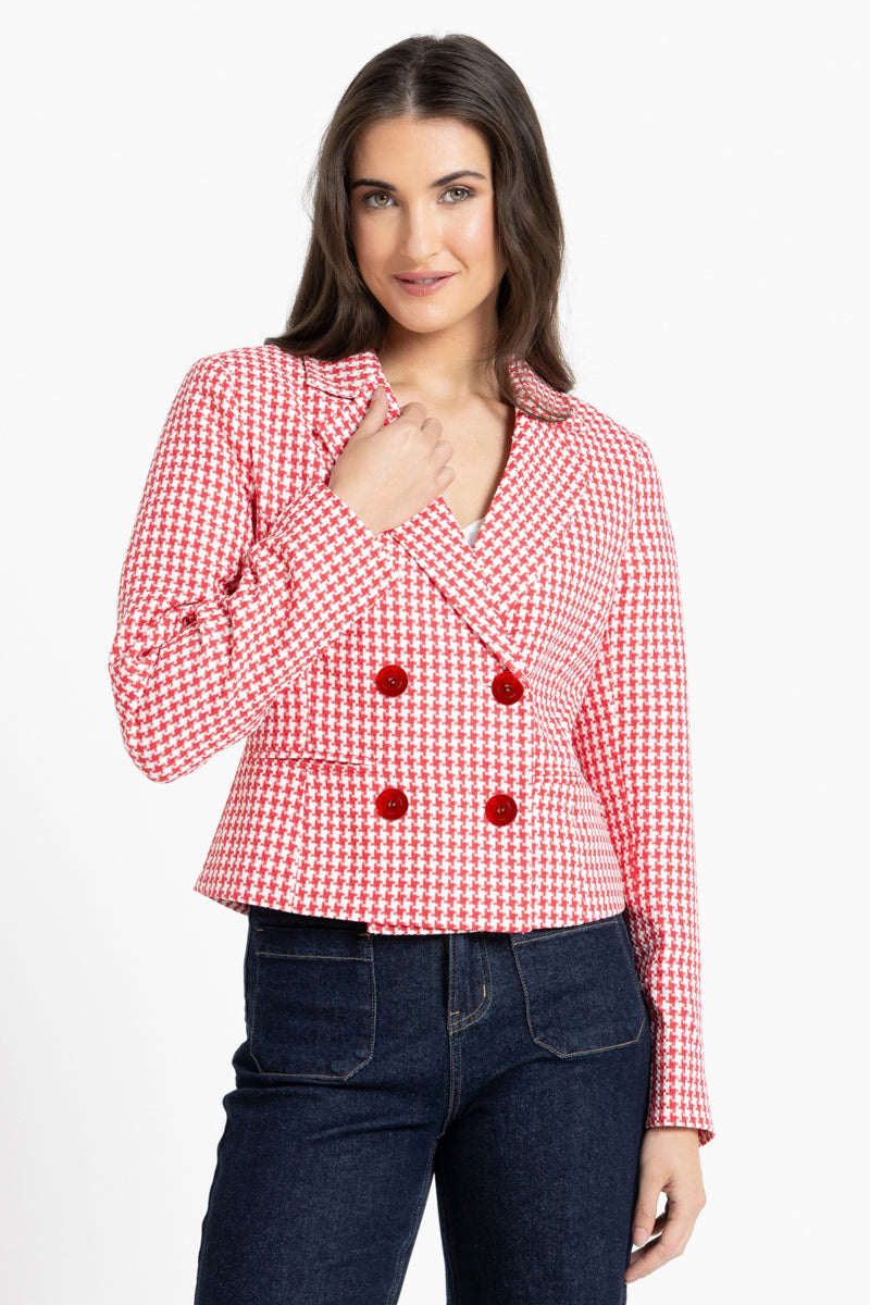 A woman modeling a red and white gingham double-breasted blazer with red buttons, paired with dark blue jeans, against a plain white background.