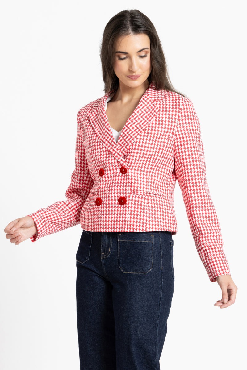A woman modeling a red and white gingham double-breasted blazer with red buttons, paired with dark blue jeans, against a plain white background.