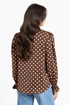 Woman wearing a brown polka dot blouse with long sleeves on a white background