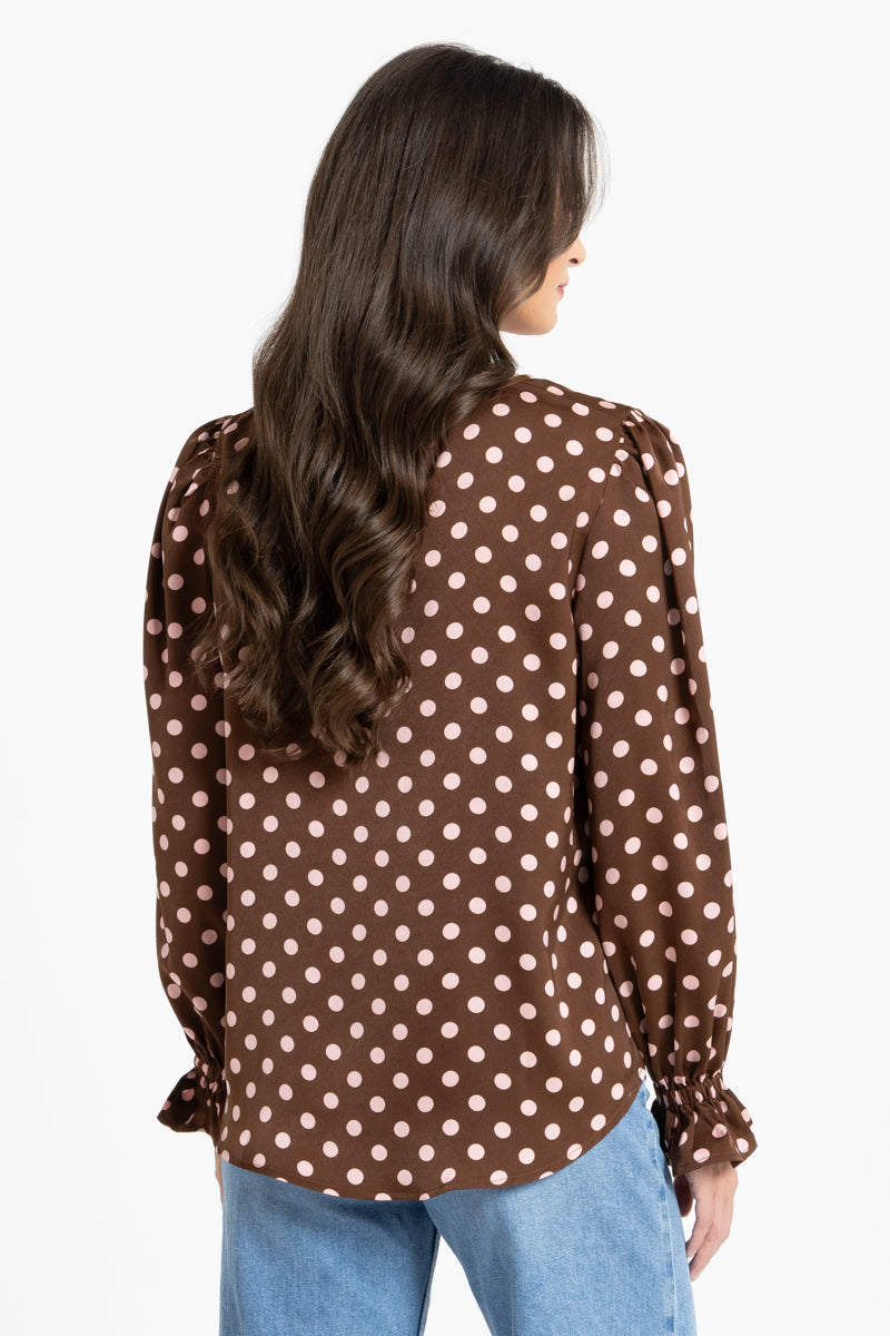 Woman wearing a brown polka dot blouse with long sleeves on a white background
