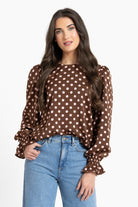 Woman wearing a brown polka dot blouse and blue jeans on a white background