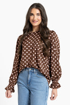 Woman wearing a brown polka dot blouse and blue jeans on a white background