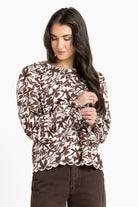 Woman wearing a brown and white floral patterned top on a white background