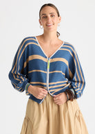 A woman modeling a blue and beige striped knit cardigan with a front zipper, paired with a beige skirt, against a plain light gray studio background.