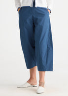 A person wearing blue cropped wide-leg pants with a white knit top and white mule flats, shown from the waist down against a plain light background.