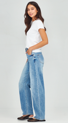 Woman wearing blue jeans and a white top on a plain background