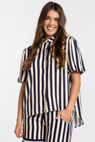 A woman modeling a matching two-piece set featuring a short-sleeve button-up blouse and shorts in a navy blue and cream vertical stripe pattern, set against a plain light gray background.