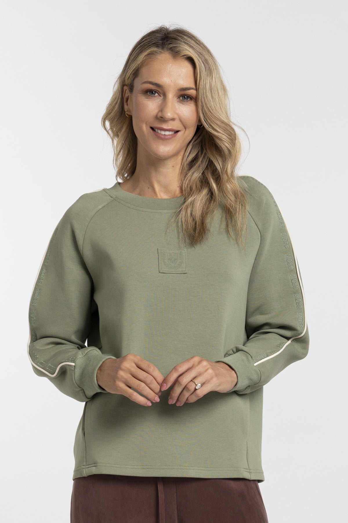 A woman wearing an olive green crewneck sweatshirt with white piping details on the sleeves, shown against a plain light gray background.