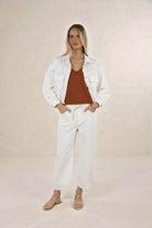 Woman wearing a white jacket and pants with a brown top against a beige background
