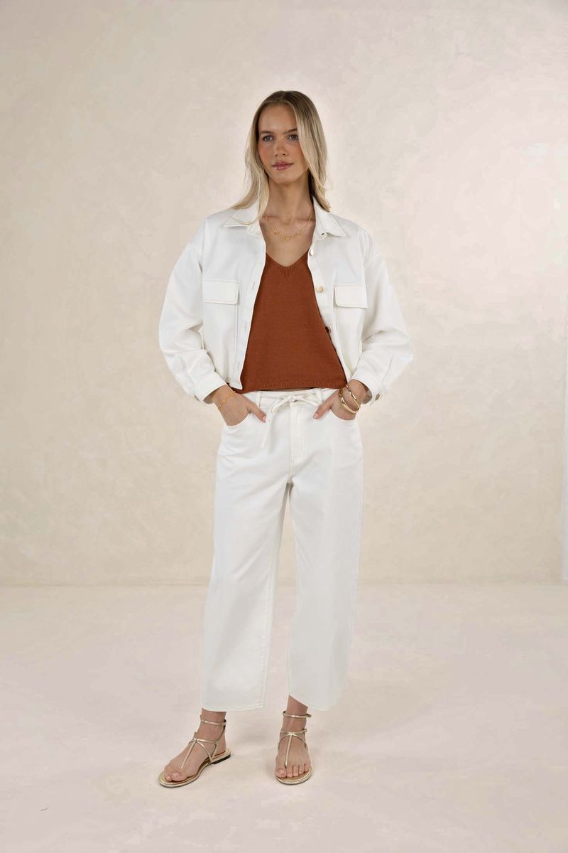 Woman wearing a white jacket and pants with a brown top against a beige background