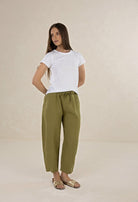 Woman wearing a white t-shirt and green pants on a beige background
