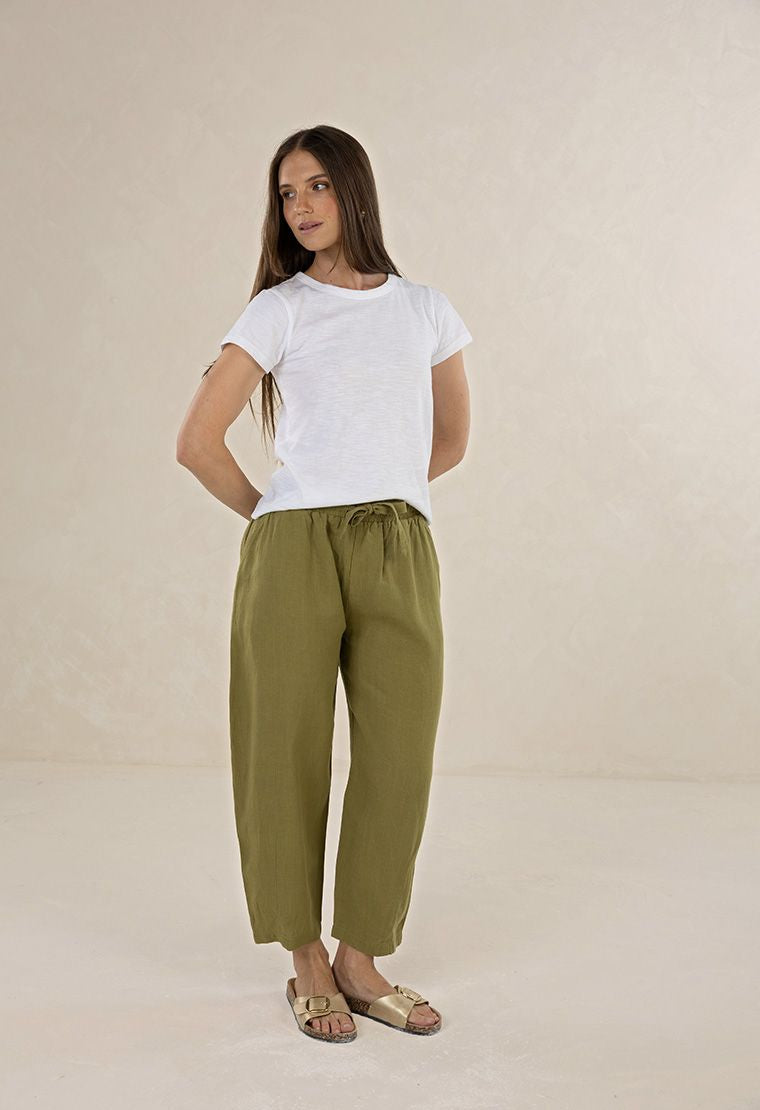 Woman wearing a white t-shirt and green pants on a beige background