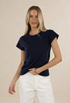 Woman wearing a navy blue t-shirt and white pants on a beige background