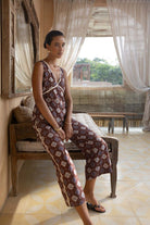 Woman in a patterned jumpsuit sitting on a bench in a room with large windows.