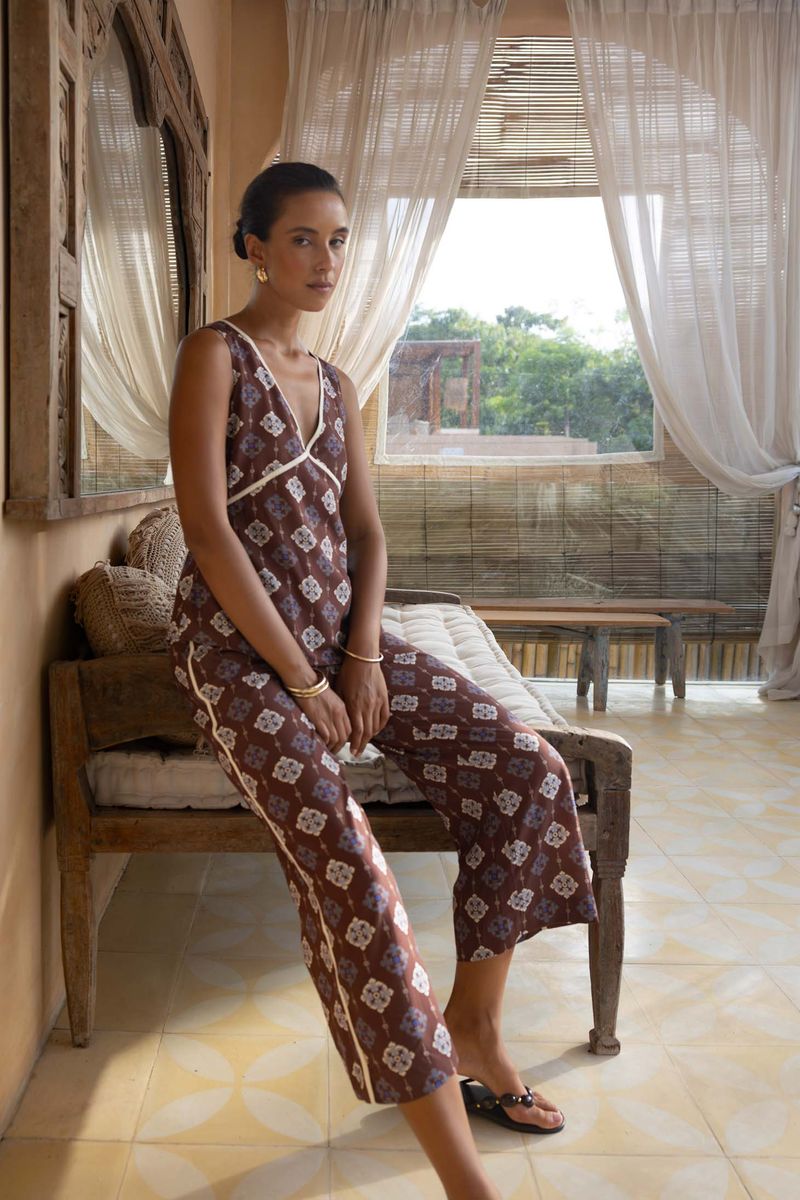 Woman in a patterned jumpsuit sitting on a bench in a room with large windows.