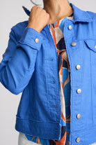 A close-up of a person wearing a bright blue denim jacket over a colorful patterned top, with the jacket's collar turned up by the hand.