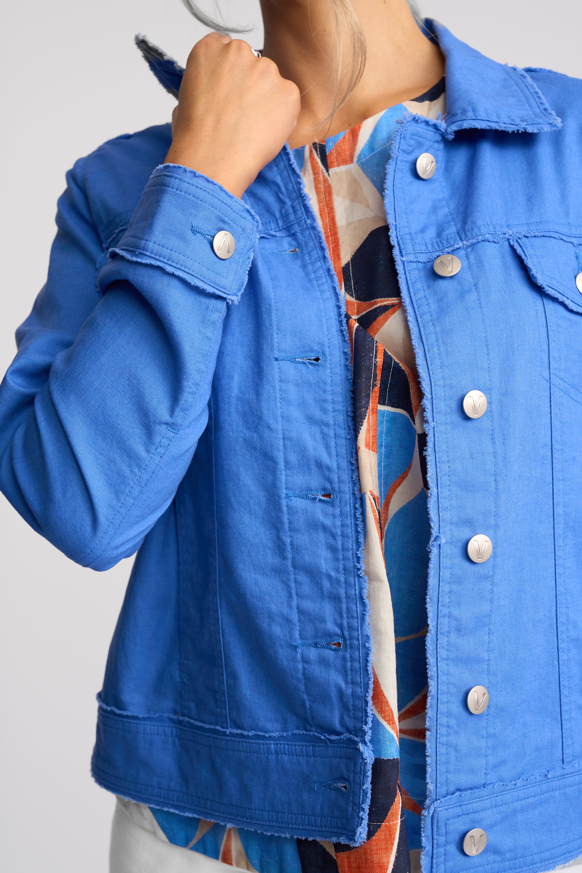 A close-up of a person wearing a bright blue denim jacket over a colorful patterned top, with the jacket's collar turned up by the hand.