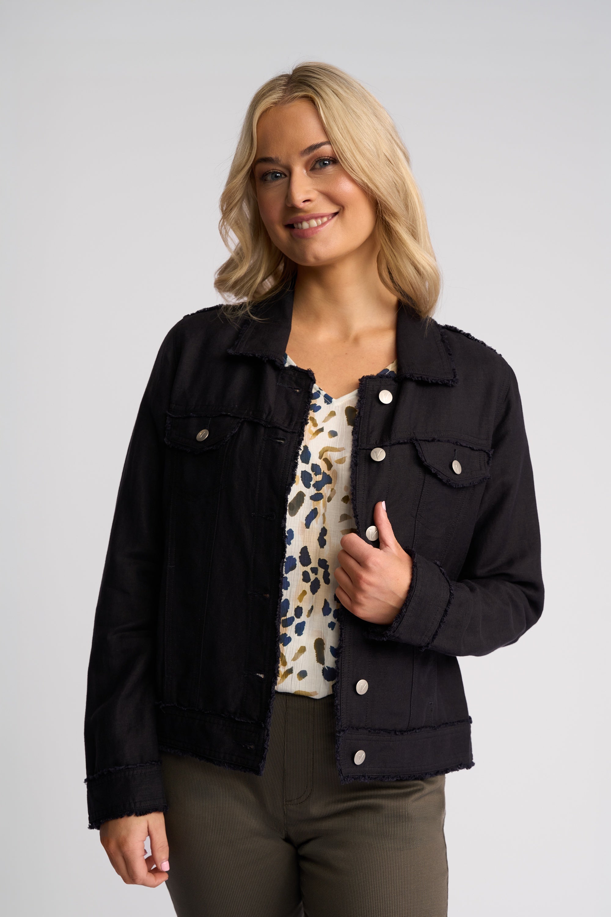 A woman modeling a black denim jacket over a leopard-print top and olive green pants, photographed against a neutral light gray studio background.