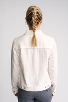 A woman viewed from behind wearing a white denim jacket and gray pants, with her blonde braid visible against a light gray studio background.