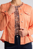 A woman wearing a coral peach ruffled jacket over a leopard print top and dark navy pants, shown from the neck down against a light gray background.