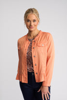 A woman modeling a coral peach cropped jacket with ruffle trim, button-front closure, and flap chest pockets, worn over a leopard-print top and dark pants against a light gray studio background.