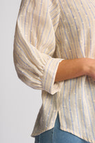 A close-up of a person wearing a cream-colored blouse with vertical blue stripes and small white dot patterns, paired with blue jeans against a light gray background.