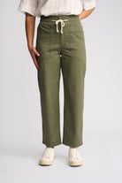 A person wearing olive green wide-leg cropped pants with a cream drawstring waist, paired with a white top and white sneakers, shown against a light gray studio background.
