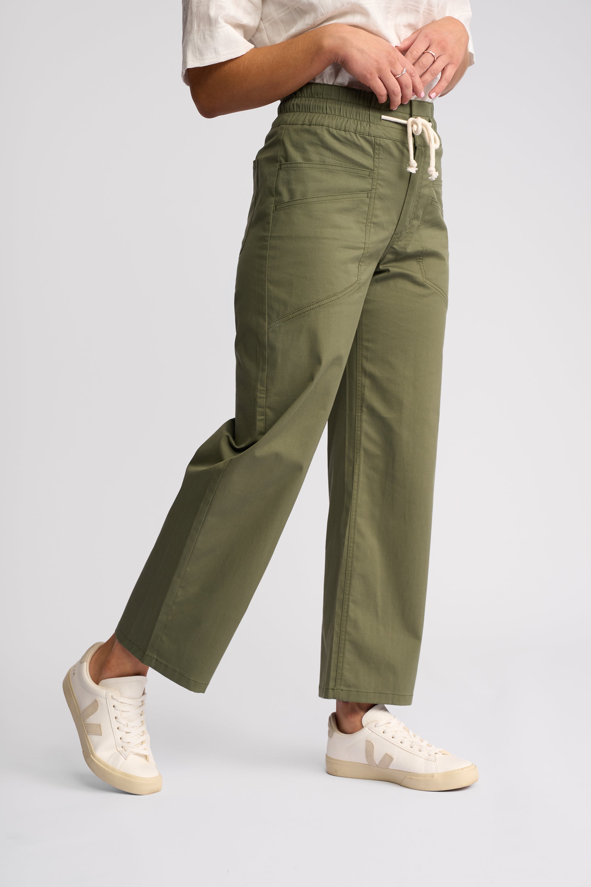 A person wearing olive green wide-leg cropped pants with a white drawstring waist, paired with white sneakers, shown against a light gray studio background.