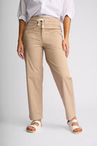 A model wearing beige drawstring trousers, a white blouse, and white slide sandals, shown from the waist down against a light gray studio background.
