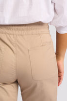 Close-up back view of a person wearing beige trousers with an elastic waistband and a side pocket, paired with a white top. The brand name 'YASSAM' is subtly embroidered on the pocket.