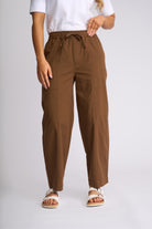A person wearing brown drawstring wide-leg pants with a white t-shirt and white slide sandals, shown from the waist down against a light gray studio background.