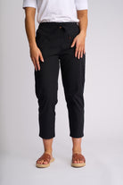 A person wearing black cropped pants with a drawstring waist, paired with a white top and brown slide sandals, photographed against a light gray studio background.