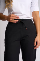 A close-up of a person wearing black drawstring trousers and a white short-sleeve top against a light gray studio background.