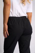 Close-up back view of a person wearing black elastic-waist pants with a white top against a light gray studio background.