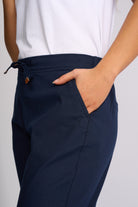 Close-up of a person wearing navy drawstring trousers with a side pocket and a white top, shown against a light gray studio background.