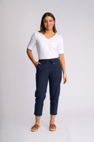 A woman modeling a pair of navy blue cropped pants with a drawstring waist, paired with a white short-sleeve V-neck top and brown slide sandals, against a light gray studio background.