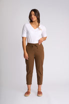 A woman modeling a white short-sleeve V-neck t-shirt and brown cropped drawstring pants against a light gray studio background.